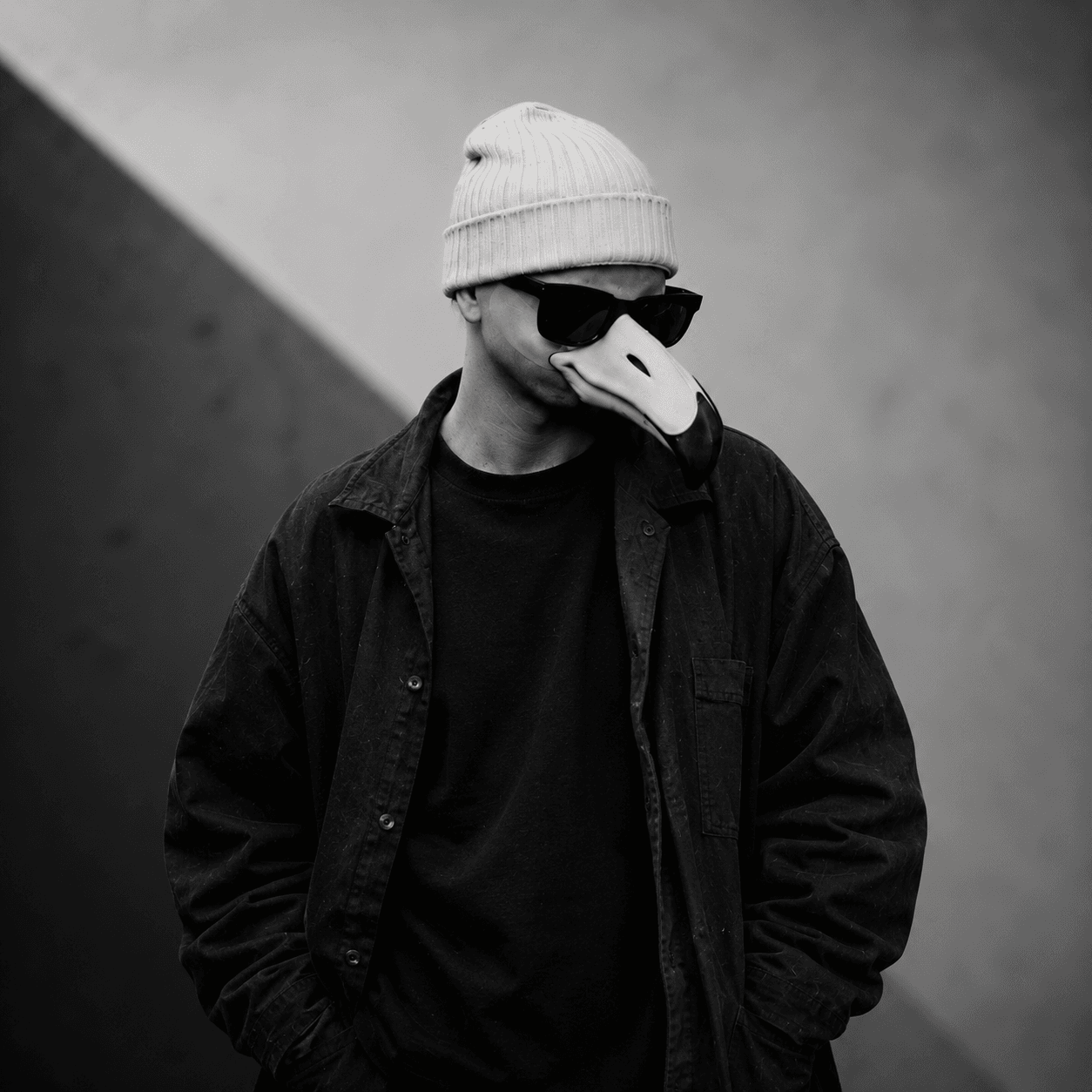 DashSounds seated outdoors, wearing a beanie, sunglasses, and his signature bird mask